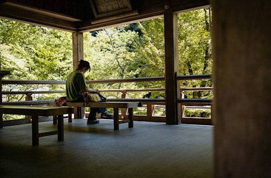 木造の東屋のベンチに座り、庭の緑を眺める人（イメージ写真）
